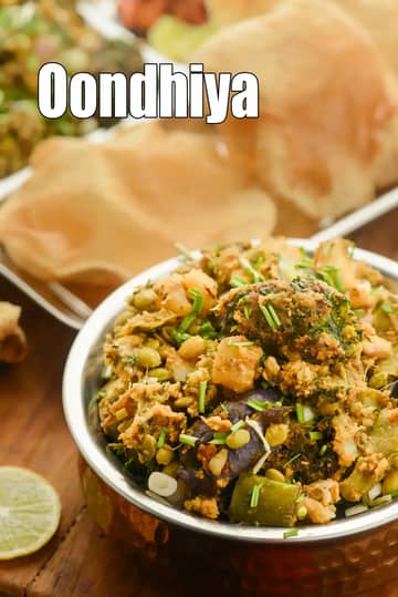 A traditional Gujarati Oondhiya served in a copper bowl, topped with fresh green herbs and served with fluffy puris in the background.