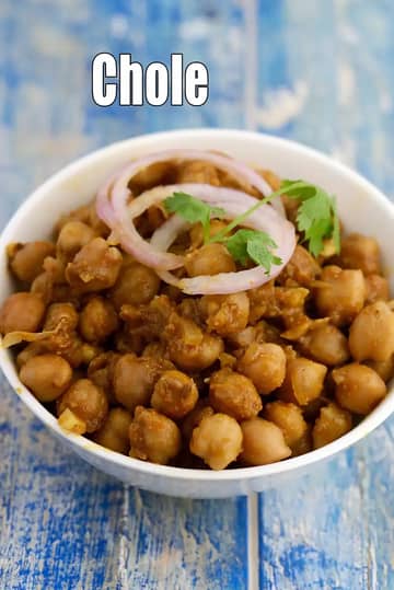 A white bowl filled with dry-style Punjabi chole, made from cooked chickpeas tossed in spices, garnished with onion rings and fresh coriander, placed on a rustic blue wooden surface.