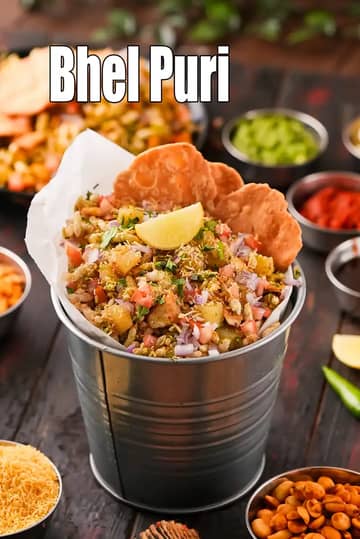 A vibrant serving of Bhel Puri presented in a small metal bucket lined with white paper, topped with a lemon wedge and crispy papdis, surrounded by small bowls of chutneys and sev.