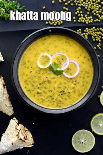 Khatta Moong curry made with whole green moong beans in a tangy yellow gravy, garnished with onion rings and coriander, served in a black bowl with lime.