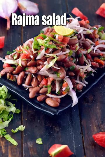 Rajma salad made with boiled kidney beans mixed with sliced onions, tomatoes, lettuce, green herbs, and lemon wedge, served in a black bowl on a rustic wooden surface.