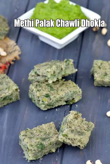 Pieces of Methi Palak Chawli Dhokla cut into small squares, made with fenugreek leaves, spinach, and black-eyed beans. Arranged on a dark wooden surface with a bowl of green chutney in the background.