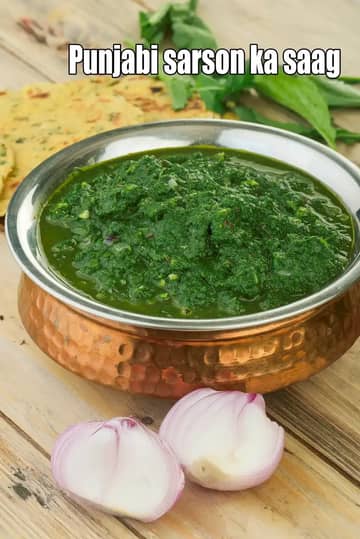 Punjabi Sarson Ka Saag served in a traditional copper bowl, garnished with mustard greens, with makki ki roti and sliced onions on a wooden table.