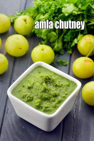 A small square white bowl filled with vibrant green Amla Chutney, surrounded by fresh whole amlas (Indian gooseberries) and green coriander leaves.