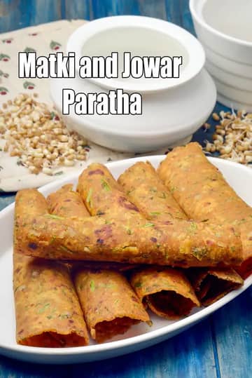 A plate of rolled Matki and Jowar Parathas arranged neatly on a white serving dish. The parathas look golden-brown and slightly crisp, with visible herbs mixed into the dough. In the background, there is a bowl of curd and a small pile of sprouted matki, placed on a rustic blue wooden surface.