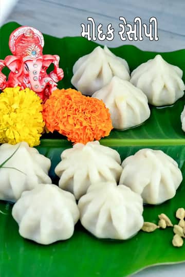 લીલા કેળાના પાન પર પીરસવામાં આવેલા પરંપરાગત સફેદ મોદક, જે કેસર અને ઘીથી સજાવેલા છે.