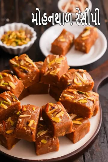 સફેદ પ્લેટમાં ગોઠવેલા મોહનથાળના ચોરસ ટુકડા, ઉપર કાપેલા બદામ અને પિસ્તાની સજાવટ સાથે, પાછળ નાના વાસણોમાં સૂકા મેવાં અને સાઇડ સર્વિંગ દેખાઈ રહ્યું છે।