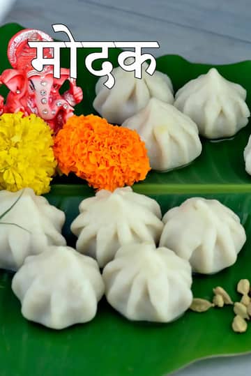 जीवंत हरे केले के पत्ते पर परोसे गए पारंपरिक सफेद उकडीचे मोदक, जिन्हें केसर और घी से सजाया गया है |