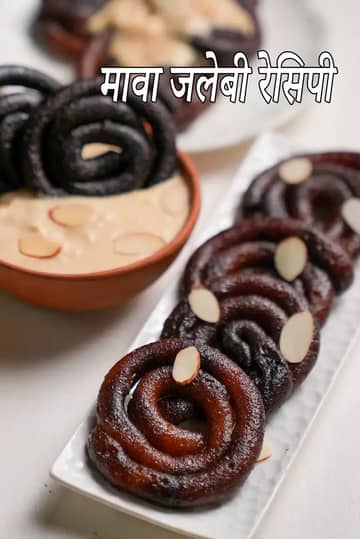 सफेद आयताकार प्लेट में सजी मावा जलेबी, गहरे भूरे रंग की सर्पिल आकार की जलेबी ऊपर से बादाम की कतरनों से सजी हुई, पीछे मलाईदार रबड़ी की कटोरी के साथ परोसी गई।