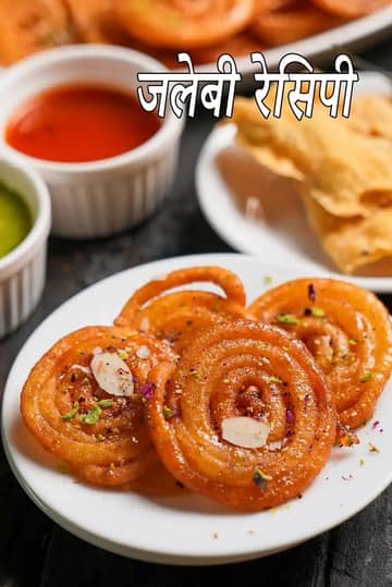 सफेद प्लेट में परोसी गई कुरकुरी और रसीली जलेबी की तस्वीर, जिसे कटे हुए बादाम, पिस्ता और गुलाब की पंखुड़ियों से सजाया गया है। बैकग्राउंड में फाफड़ा की एक प्लेट और लाल व हरी चटनी की कटोरियाँ दिखाई दे रही हैं। यह तस्वीर पारंपरिक भारतीय नाश्ते के बेहतरीन मेल को दर्शाती है।