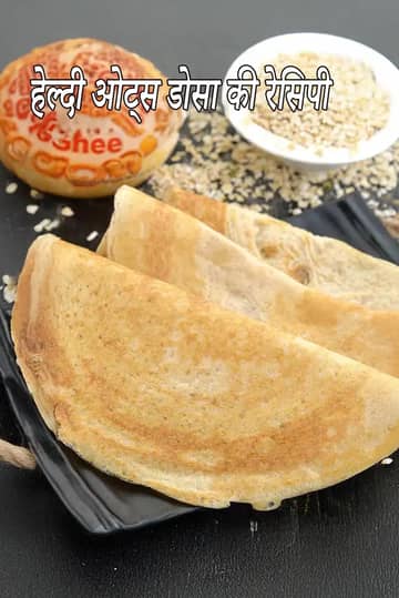 एक काली प्लेट पर आधे चाँद के आकार में मुड़े हुए तीन कुरकुरे, सुनहरे-भूरे ओट्स डोसा, और बैकग्राउंड में कच्चे ओट्स का एक छोटा कटोरा।