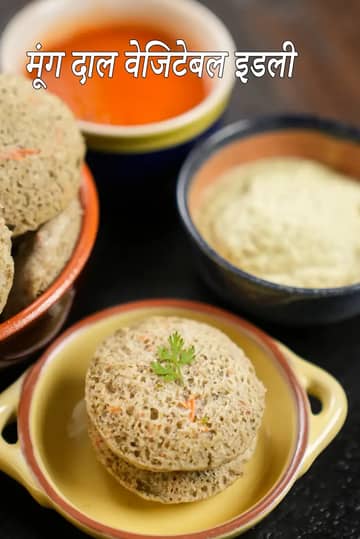 ग्रीन मूंग दाल और सब्ज़ियों से बनी इडली पीले सिरेमिक कटोरे में सजी हुई है, ऊपर धनिया से सजाई गई है और साथ में छोटे कटोरों में नारियल की चटनी और लाल चटनी परोसी गई है।