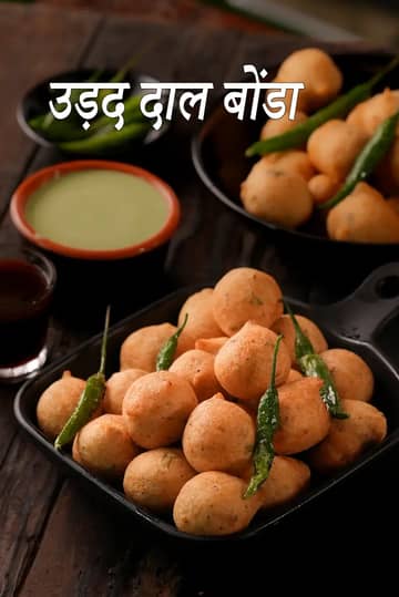 सुनहरे-भूरे और कुरकुरे तले हुए उड़द दाल बोंडा, जिन्हें एक कटोरे में परोसा गया है। इनके साथ तीखी नारियल की चटनी और ताजी हरी मिर्च रखी हुई है।