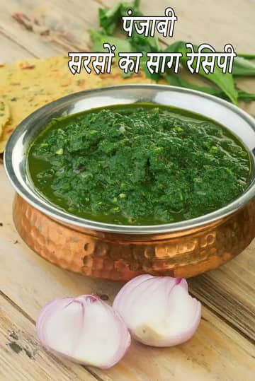 तांबे के बर्तन में परोसा गया पंजाबी सरसों का साग, साथ में मक्की की रोटी और कटी हुई प्याज़, लकड़ी की मेज़ पर रखा हुआ।