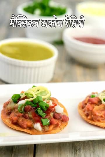 एक सफेद प्लेट पर परोसे गए दो कुरकुरे मैक्सिकन टैकोस  का क्लोज-अप शॉट। टैकोस के ऊपर लाल बीन्स (राजमा) की फिलिंग, कटे हुए सफेद प्याज, ताजी हरी प्याज  और लाल साल्सा डाली गई है। बैकग्राउंड में हरी चटनी और लाल सॉस से भरी छोटी सफेद कटोरियाँ दिखाई दे रही हैं, जो इसे एक रंगीन और स्वादिष्ट भोजन बनाती हैं।