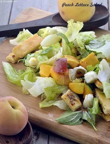A fresh Peach Lettuce Salad is served on a wooden cutting board. The salad contains crispy lettuce leaves, ripe peach chunks, cubes of paneer or cheese, and fresh basil leaves. Two whole peaches are placed nearby, and a wooden spoon rests in the background. The salad looks colorful, healthy, and appetizing.