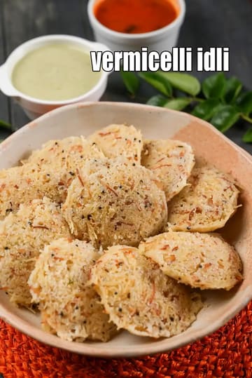 A bowl of soft vermicelli idli made from roasted semiya, garnished with mustard seeds and spices, served with coconut chutney and red chutney in the background on a dark surface.