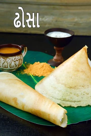 આ ચિત્રમાં કેળાના લીલા પાન પર બે પ્રકારના ઢોસા બતાવવામાં આવ્યા છે—એક રોલ કરેલો અને બીજો શંકુ (કોન) આકારનો। તેની સાથે એક કપમાં સાંભર, થોડો તીખો ચટણી પાવડર અને એક ઘેરા રંગના બાઉલમાં સફેદ નારિયેળની ચટણી પીરસવામાં આવી છે.