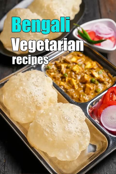 Bengali vegetarian meal served in a stainless steel thali with puffed luchi, paneer curry, sliced onions, tomatoes, and green chilli on a wooden table.