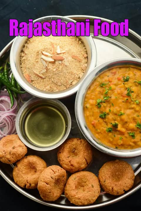 Rajasthani food platter served in a traditional steel thali featuring dal, churma garnished with almonds, ghee in a small bowl, and baati, accompanied by sliced onions and green chilies, with the text Rajasthani Food displayed on the image.