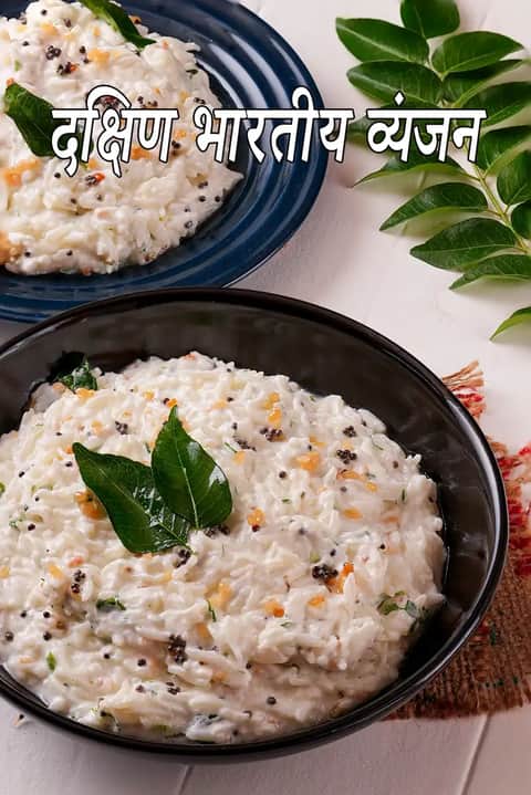 काले बाउल में परोसी गई दक्षिण भारतीय दही चावल, ऊपर से करी पत्ते, राई और दाल के तड़के से सजी हुई, हल्के बैकग्राउंड पर रखी गई है और तस्वीर परदक्षिण भारतीय व्यंजन लिखा हुआ दिखाई देता है।