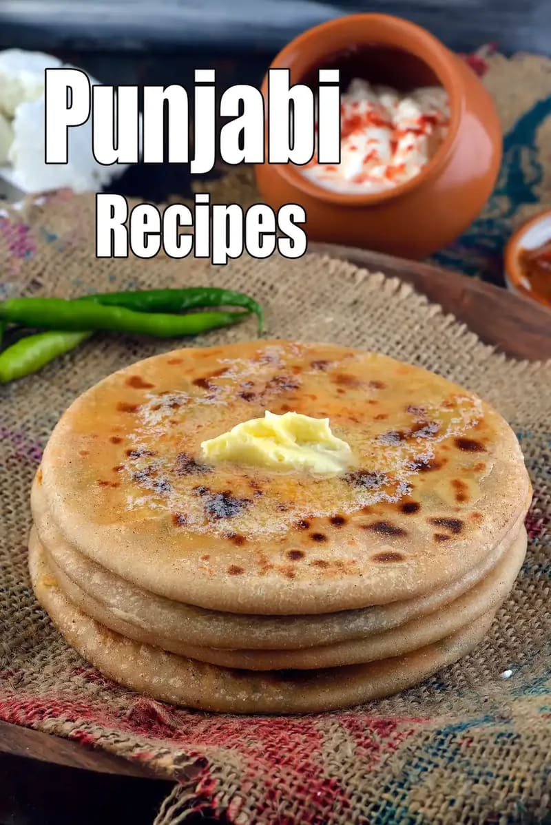 A stack of freshly cooked Indian stuffed flatbreads (parathas) topped with a dollop of butter, served on a rustic cloth with green chilies, curd, and pickle on the side.