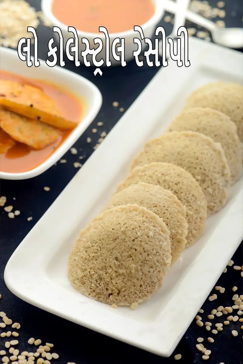 એક લાંબી સફેદ લંબચોરસ પ્લેટમાં નરમ અને બાફેલા ઓટ્સ ઈડલી સરસ રીતે ગોઠવેલા છે. પાછળના ભાગમાં બે બાઉલ છે: એકમાં ચટકાદાર નારંગી રંગની ટામેટાની ચટણી છે અને બીજામાં અન્ય એક સ્વાદિષ્ટ વાનગી છે. આ બધું એક ઘેરા રંગના ટેબલ પર રાખેલું છે, જેની આસપાસ થોડી કાચી દાળ અથવા અનાજ વેરાયેલા છે જે હેલ્ધી ઘટકો સૂચવે છે. ચિત્રની ઉપર મોટા સફેદ અક્ષરોમાં લખ્યું છે, લો કોલેસ્ટ્રોલ ઇન્ડિયન રેસિપીઝ.