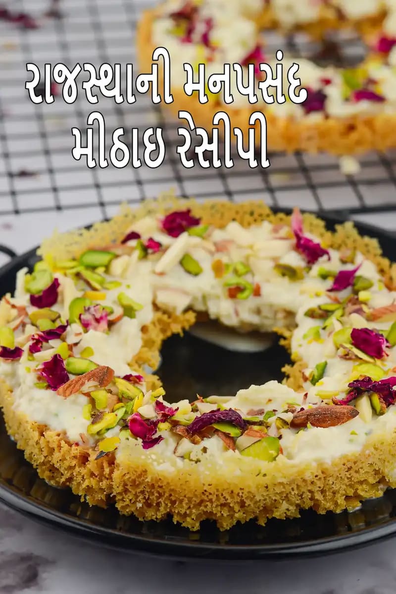 સોનેરી બેઝ પર ક્રીમી સફેદ પરતવાળી રાજસ્થાની મીઠાઈ, પિસ્તા, બદામ અને ગુલાબની પાંખડીઓથી સજાવેલી, કાળી થાળીમાં પીરસેલી, અને તસવીર પર “Rajasthani Mithai Recipes” લખાણ દર્શાવવામાં આવ્યું છે।