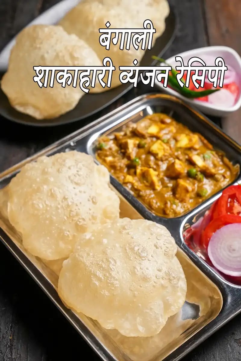 लकड़ी की मेज़ पर रखी स्टेनलेस स्टील थाली में परोसा गया बंगाली शाकाहारी भोजन, जिसमें फूली हुई लूची, पनीर की सब्ज़ी, कटे हुए प्याज़, टमाटर और हरी मिर्च शामिल हैं।