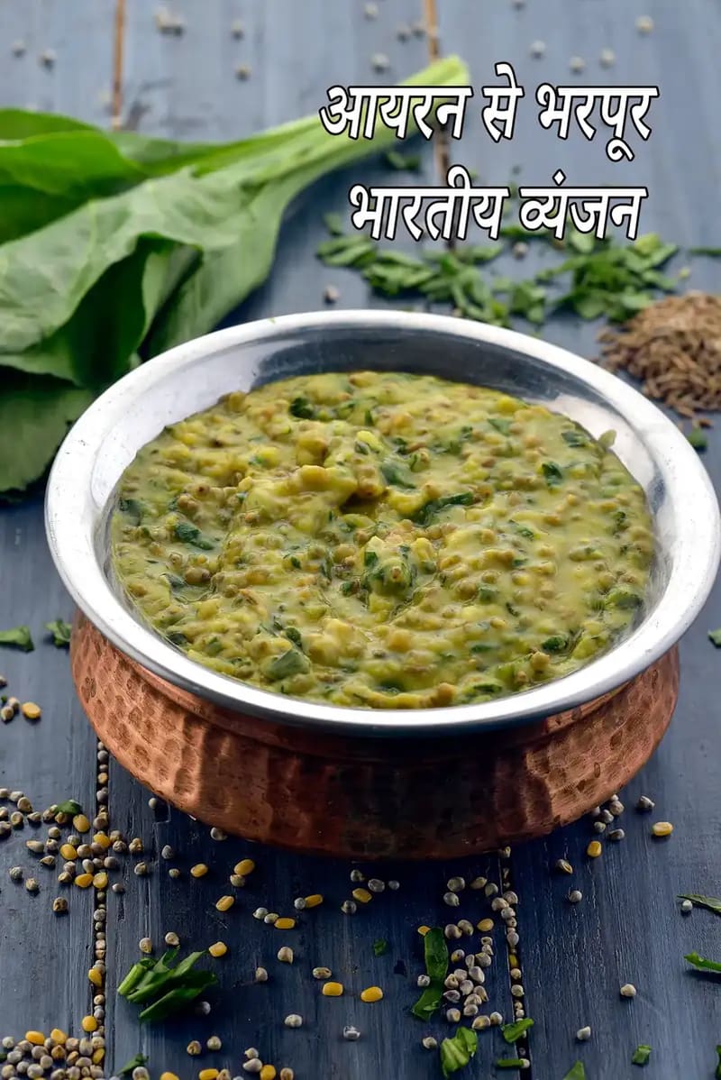 गहरे नीले लकड़ी की सतह पर रखे एक पारंपरिक तांबे के कटोरे में पौष्टिक पालक और दाल दिखाई दे रही है। यह डिश गाढ़ी और स्वास्थ्यवर्धक लग रही है, जिसमें बारीक कटा हुआ पालक और दाल के दाने साफ देखे जा सकते हैं। कटोरे के चारों ओर कच्ची दालें, बीज और ताज़ा हरा धनिया बिखरा हुआ है। बैकग्राउंड में ताज़ा पालक की पत्तियाँ और जीरे का ढेर सामग्री की शुद्धता को दर्शाता है। ऊपर बड़े सफेद अक्षरों में लिखा है,आयरन से भरपूर भारतीय रेसिपीज़।