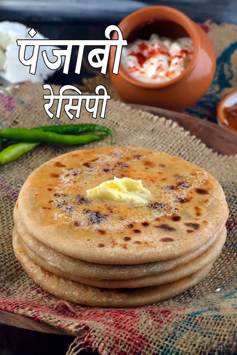 मक्खन से सजी हुई ताज़ी बनी हुई भारतीय स्टफ्ड पराठों की एक परतदार ढेरी, जिसे देसी कपड़े पर परोसा गया है, साथ में हरी मिर्च, दही और अचार रखा है।