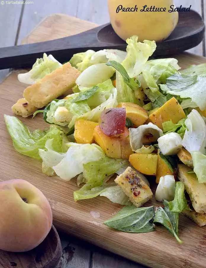 A fresh Peach Lettuce Salad is served on a wooden cutting board. The salad contains crispy lettuce leaves, ripe peach chunks, cubes of paneer or cheese, and fresh basil leaves. Two whole peaches are placed nearby, and a wooden spoon rests in the background. The salad looks colorful, healthy, and appetizing.